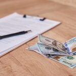 document, pen and dollar bills on table, close up